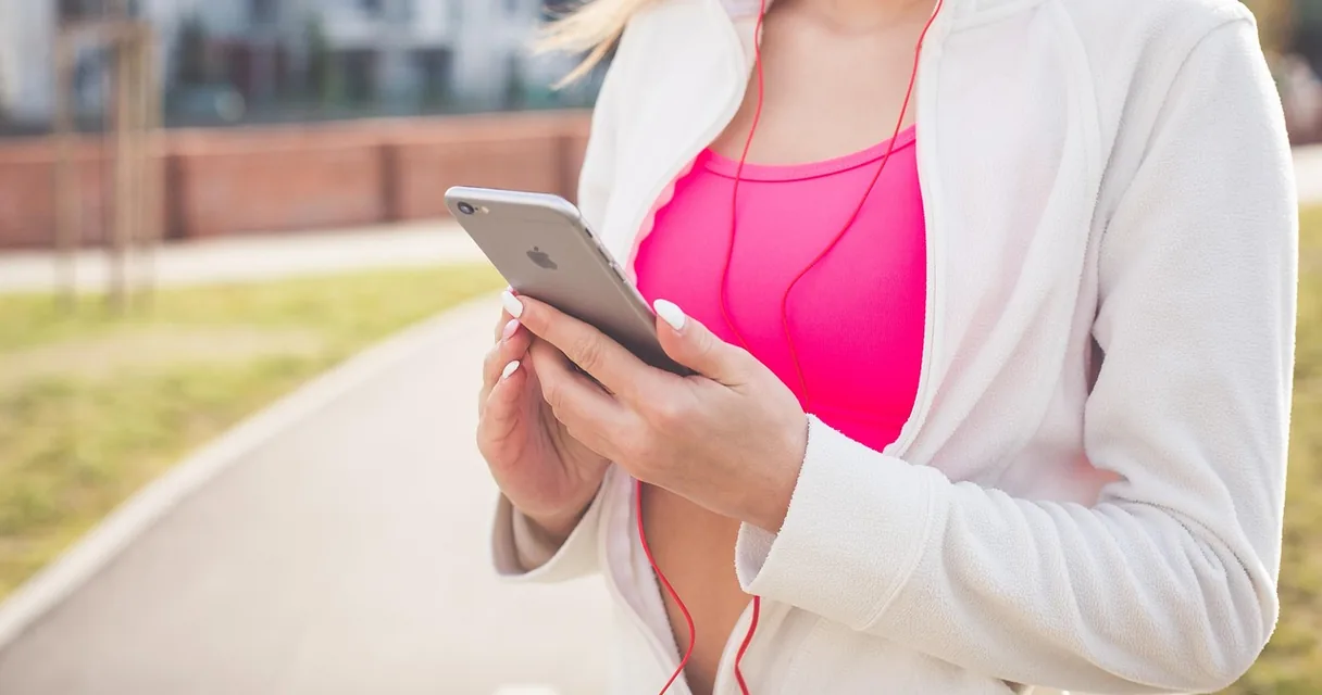 Mulher com fones de ouvido vermelhos segurando um celular durante uma caminhada, ilustrando o audiolivro no celular